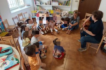 Bambini seduti per terra in cerchio che ascoltano un adulto che suona la chitarra